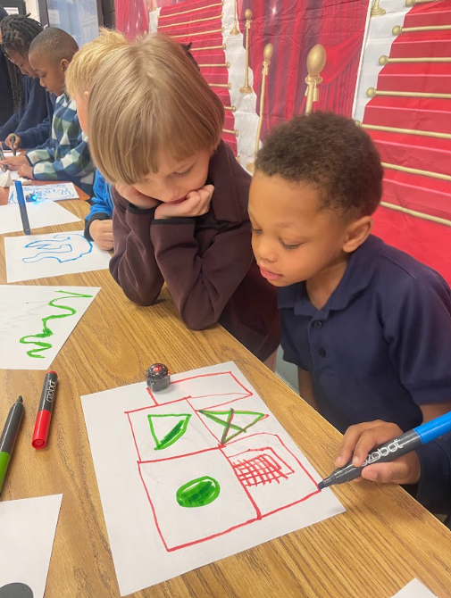 2 Students looking at drawings on a piece of paper. The drawings depict a path of which the students created for their robot to follow 
