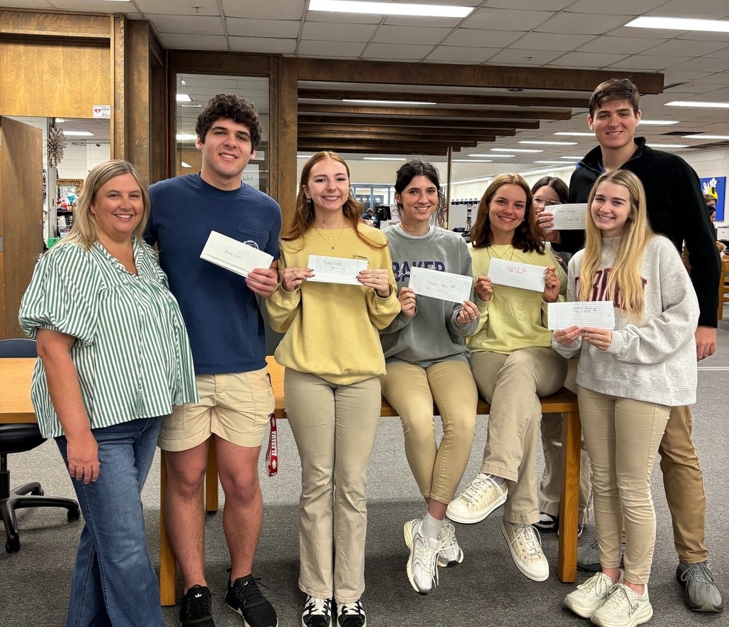 Several Baker High seniors, holding letters and standing with a teacher