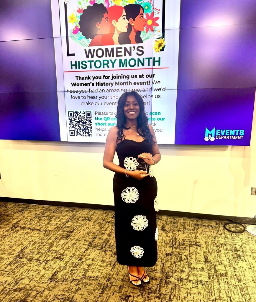 Lakenda Craig holds an award in front of a screen promoting Women's History Month