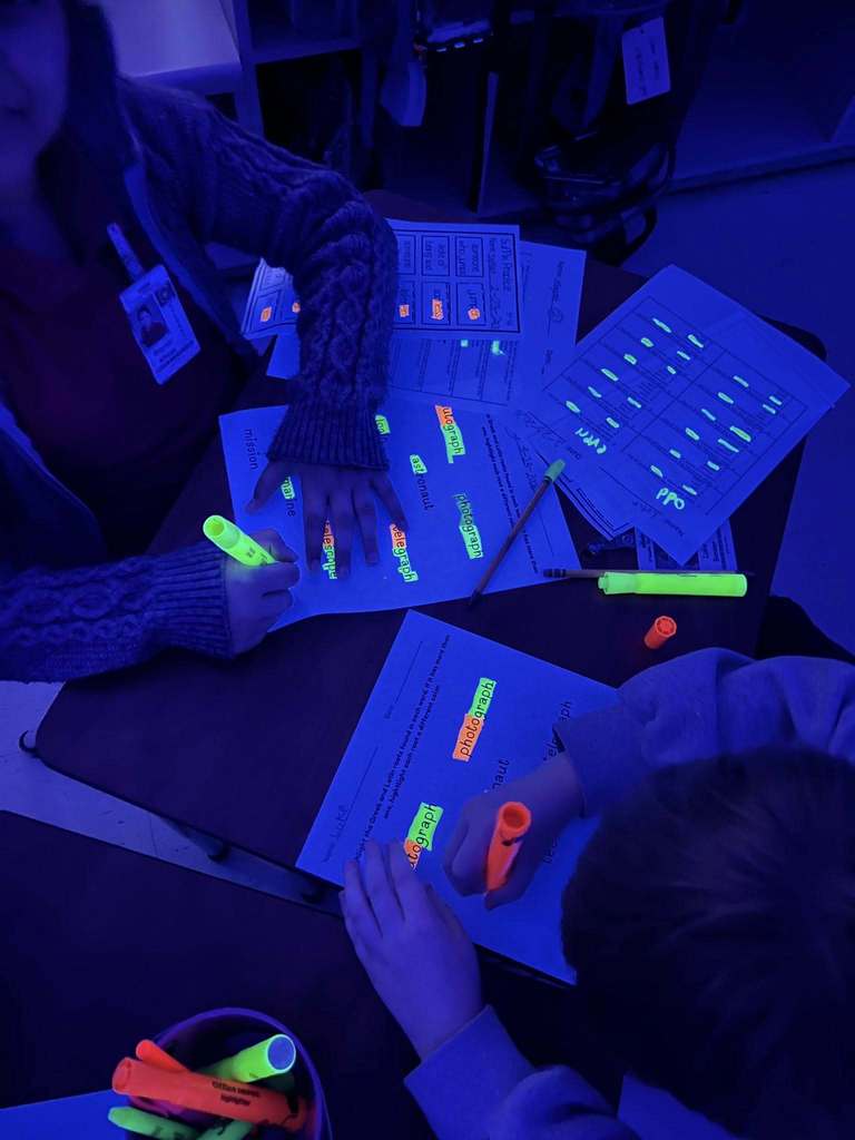 O'Rourke Elementary students marking worksheets with glowing highlighters in a black-lit room
