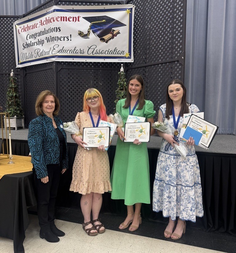 A woman stands with three high school girls, who are holding certificates