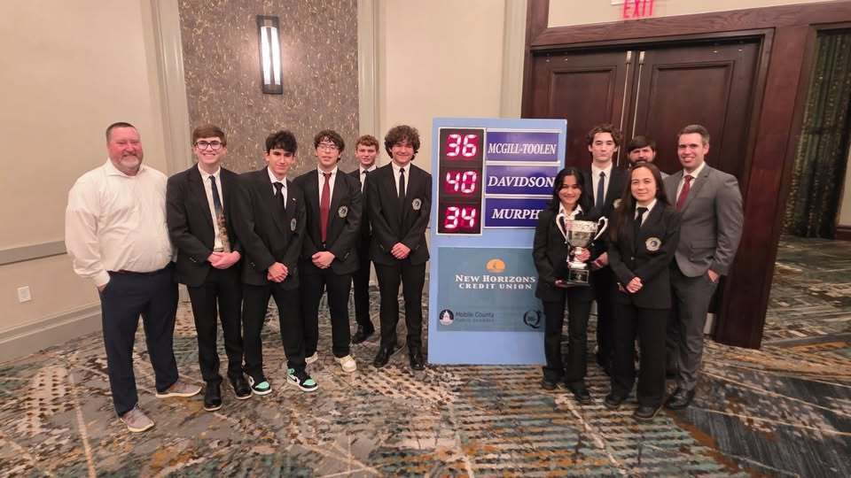 Davidson's Hi-Q team, standing with a trophy in front of the scoreboard for the championship match