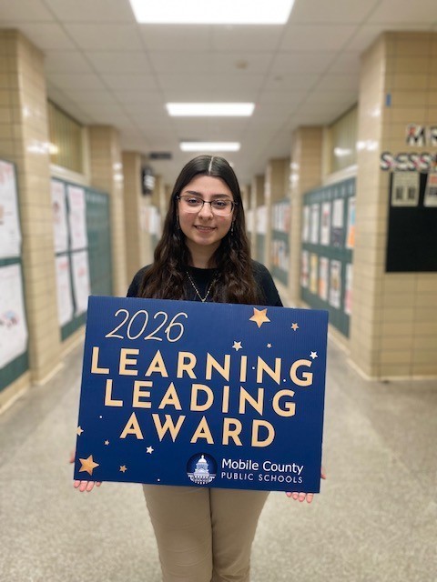 Farah Hujier holds a Learning Leading Award sign in a hallway