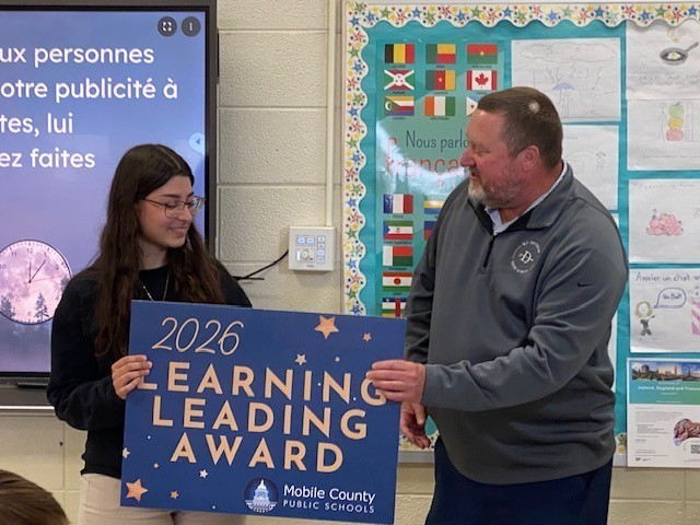Davidson Principal Jason Richardson hands Farah Hujier a Learning Leading Award sign