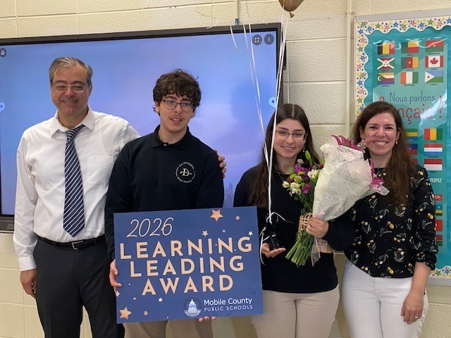 Farah Hujier holds a Learning Leading Award sign and stands with her parents and brother