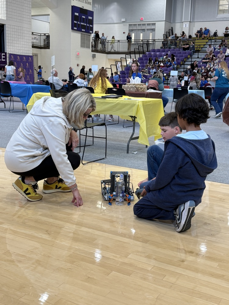 two students and judges kneel beside a student built robot on gym floor