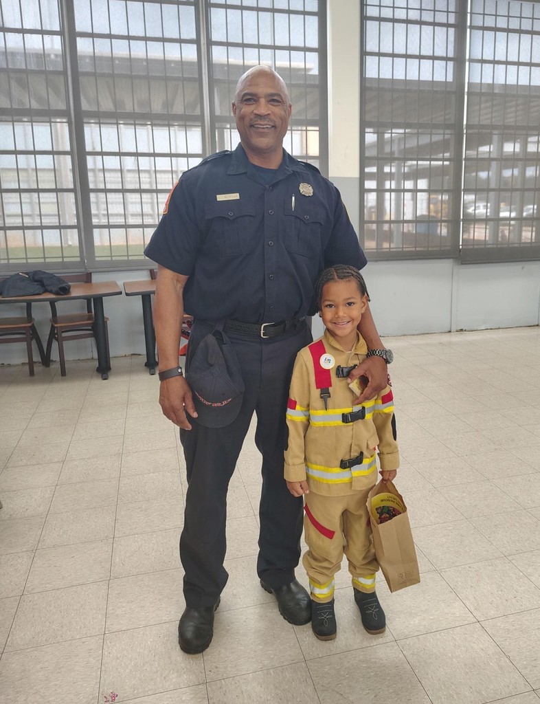 A boy dressed as a firefighter stands with a real firefighter