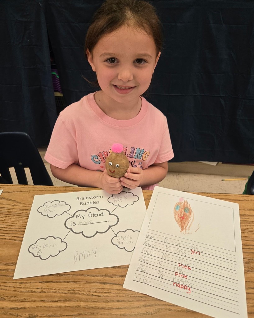 A girl holds a potato with a smiley face on it, with worksheets on the table in front of her