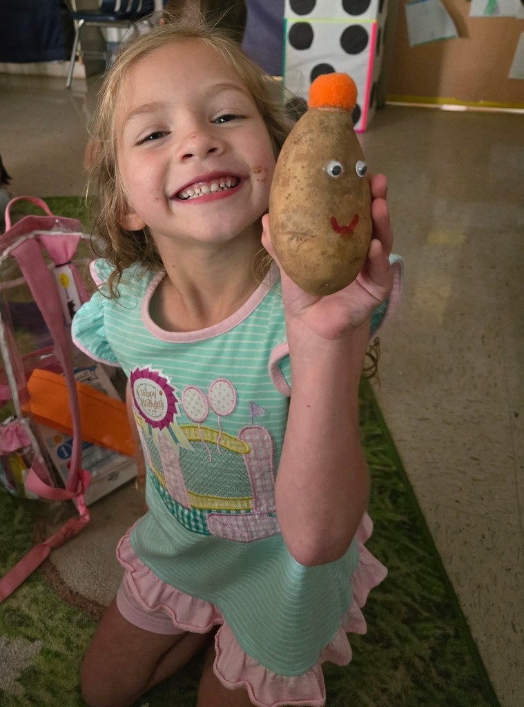 A smiling girl holds a potato with a smiley face on it