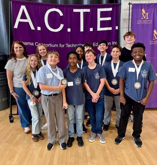 A group of students and a teacher in front of an ACTE backdrop