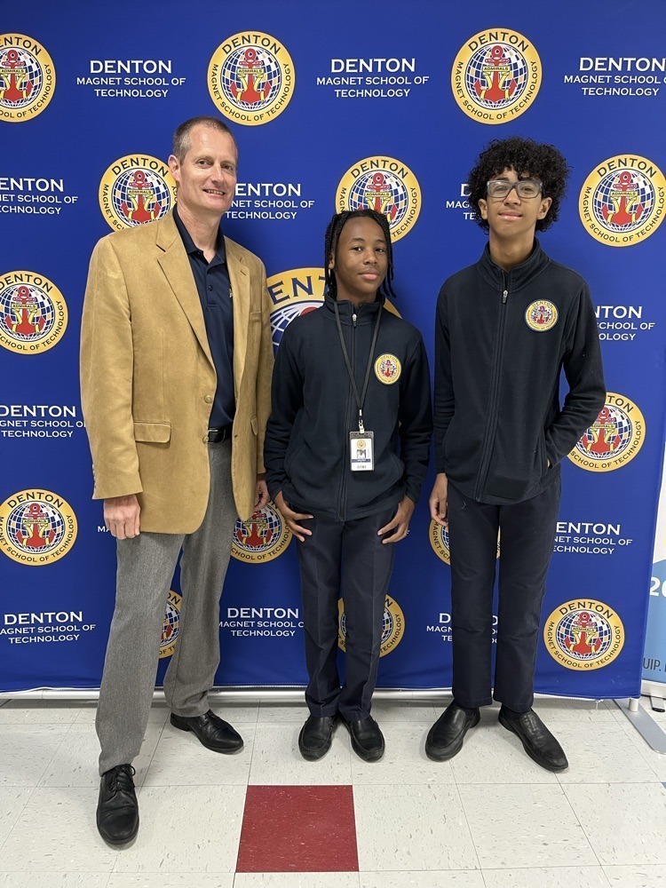 Two students and a principal in front of a Denton backdrop