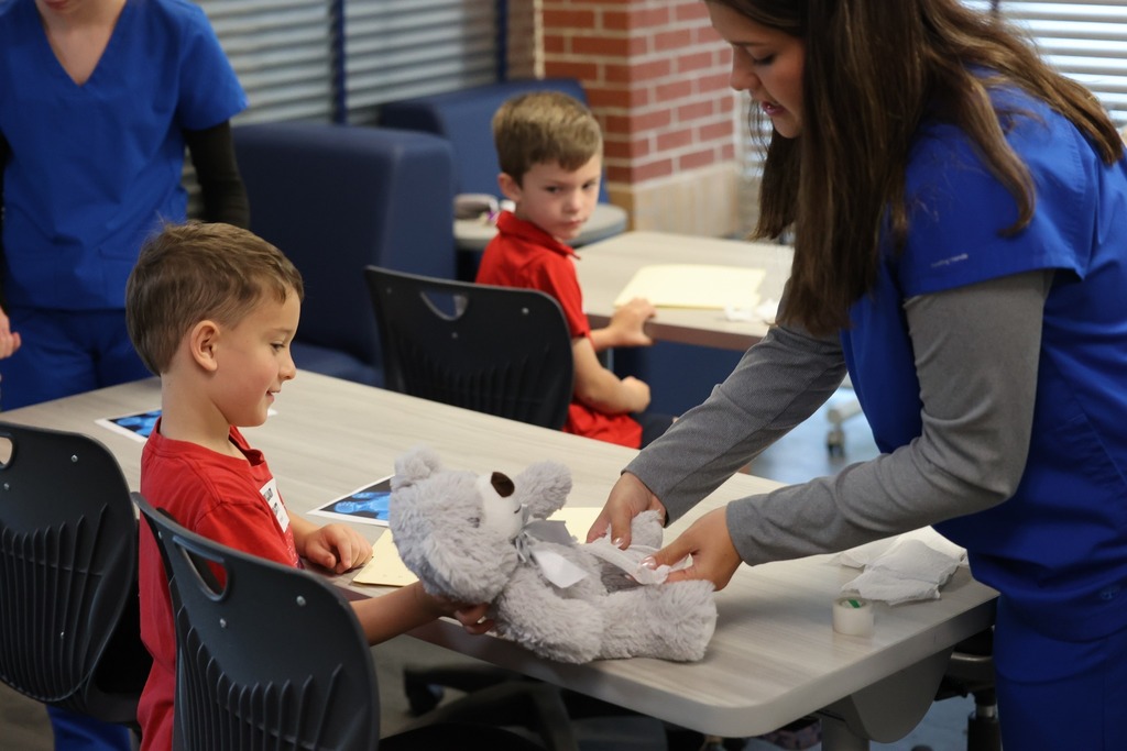 A Bryant High student bandaging a teddy bear as a Castlen Elementary student watches