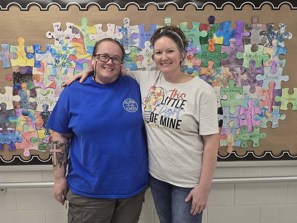 Two teachers standing in front of a bulletin board decorated with puzzle pieces