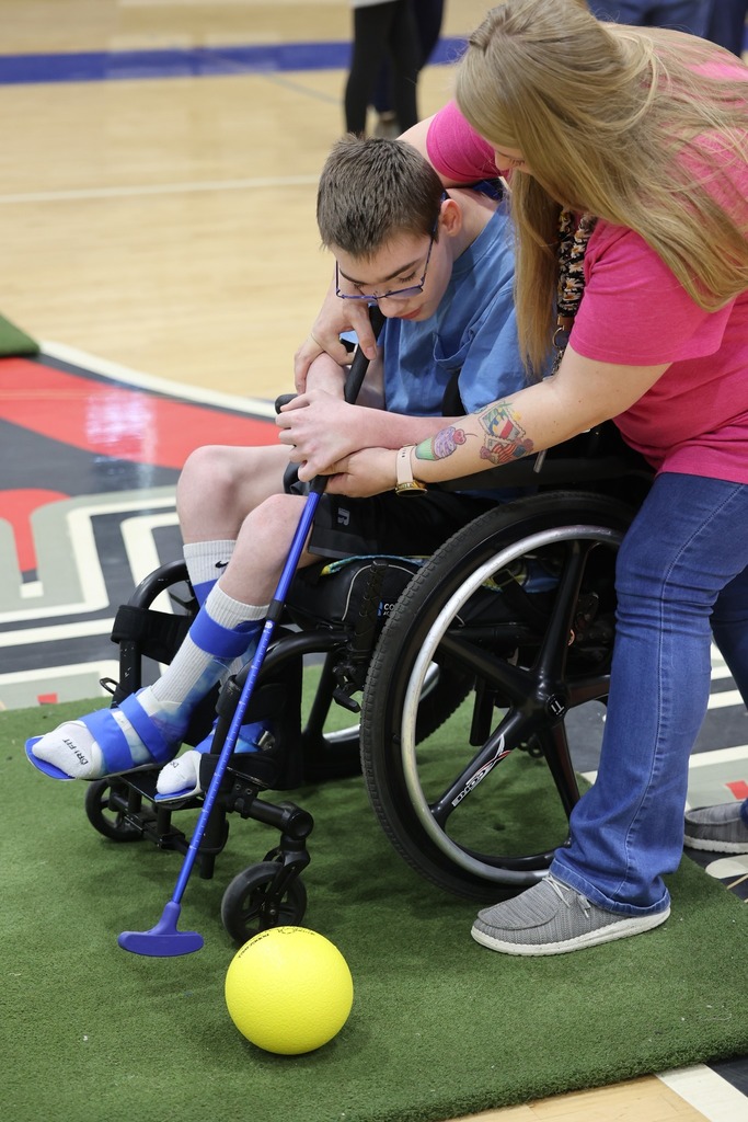 A woman helping a boy in a wheelchair hit a ball with a putter
