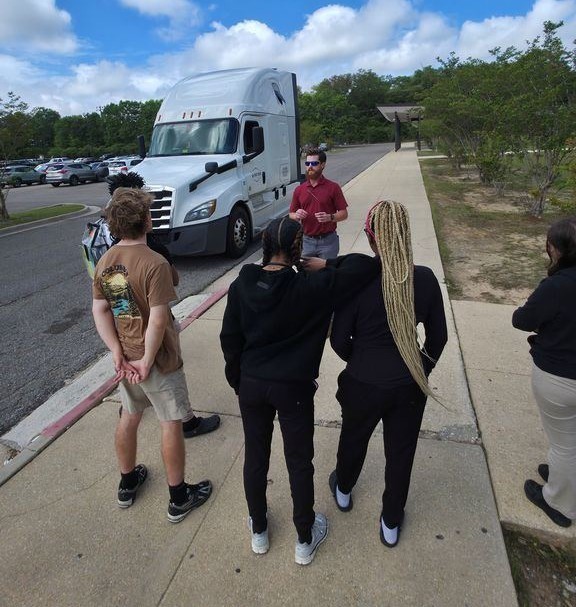 A man talks with several Theodore High students in front of a semi truck