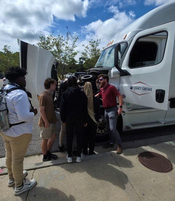 A man shows a truck engine to Theodore High students