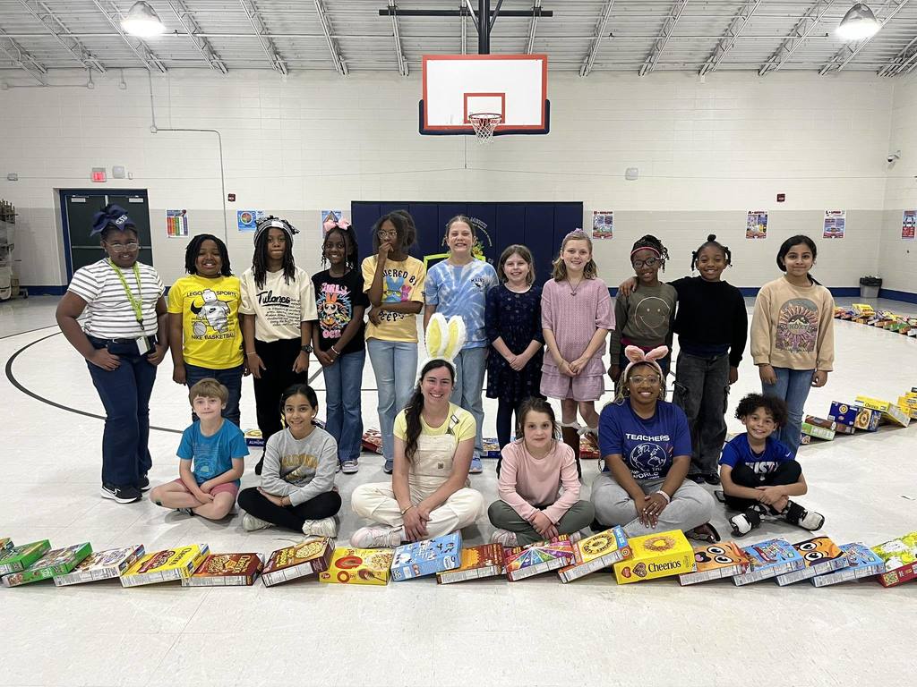 Two teachers and a group of Eichold-Mertz students posing with cereal boxes in a gymnasium