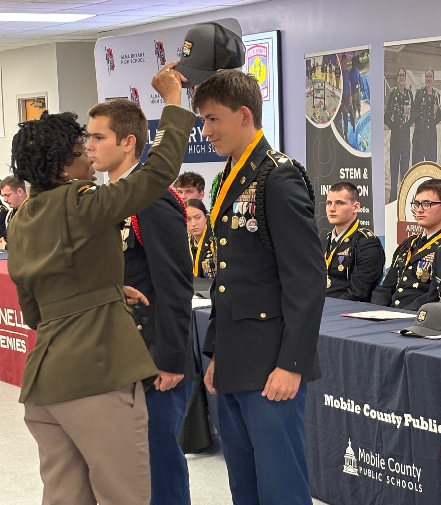 A JROTC instructor placing a cap atop a cadet's head