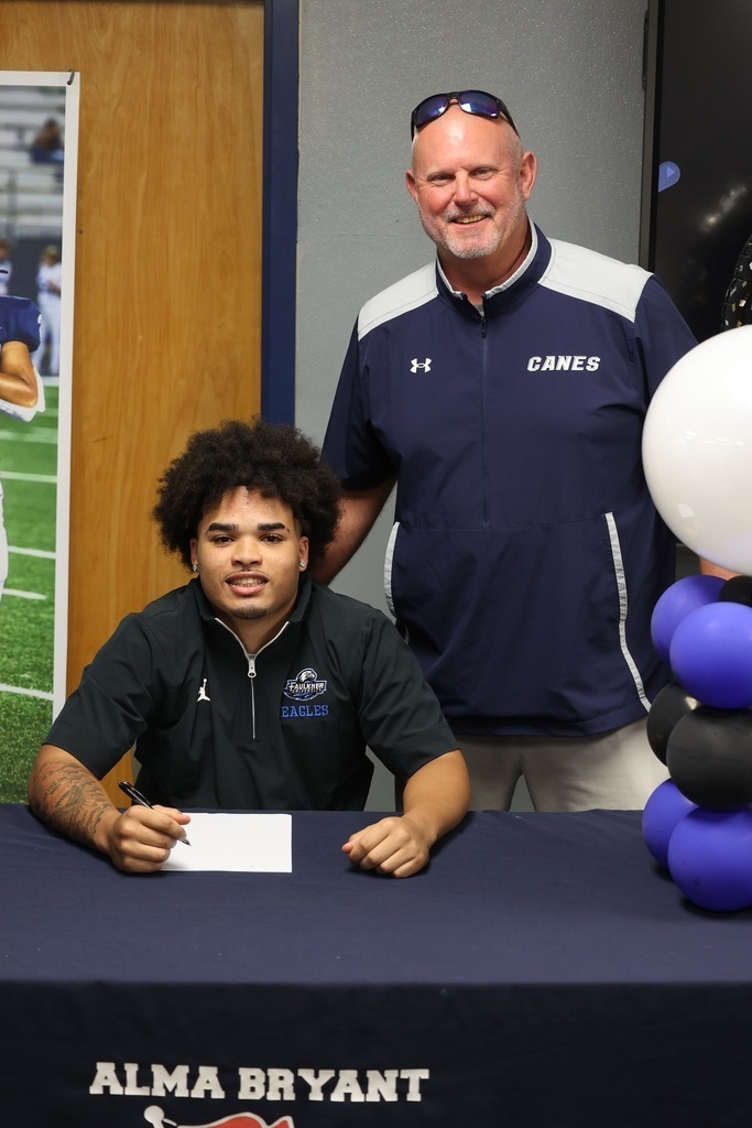 An Alma Bryant student sits at a table while football coach Bart Sessions stands behind him