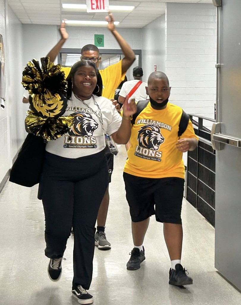 A smiling Williamson teacher leads a student down a hallway