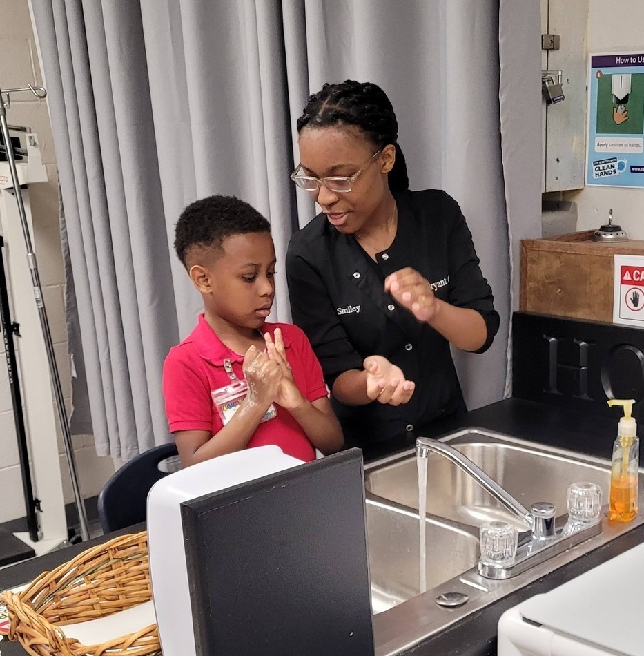 A high school student watches a kindergartener washing his hands