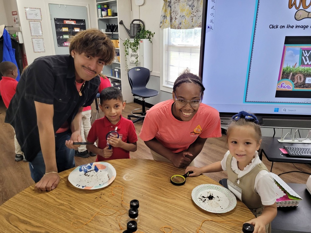 Two high school students stand by a table with two kindergarteners