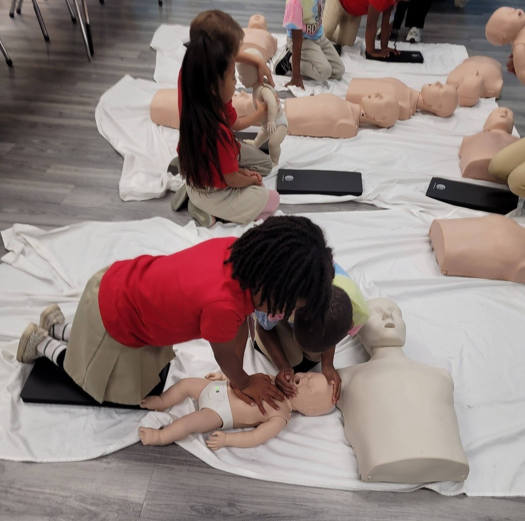 Two kindergarteners try CPR methods on a doll
