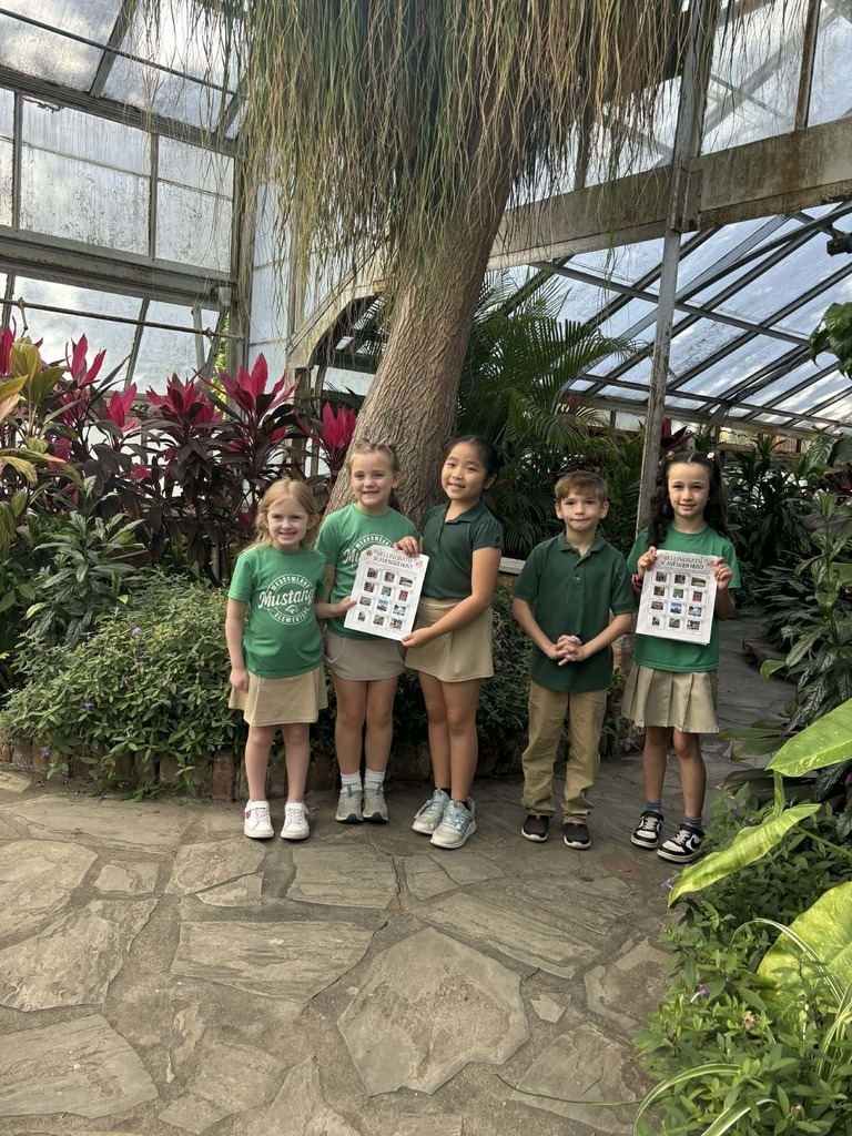 Meadowlake students standing inside a tropical greenhouse holding up posters about pollinators.