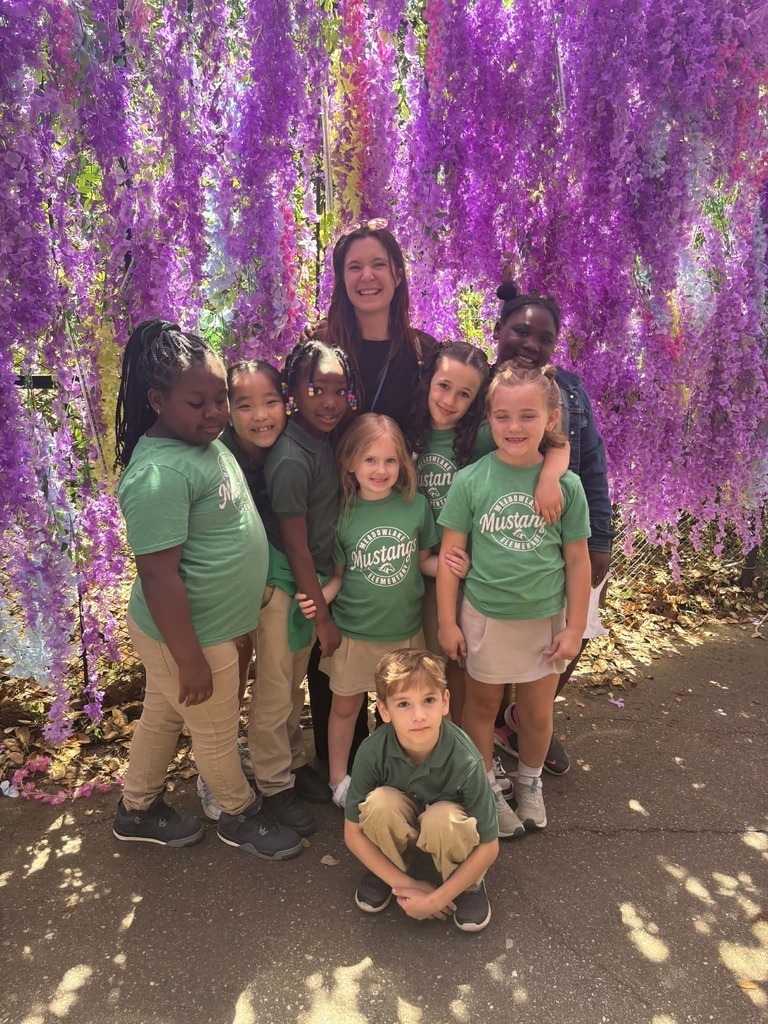 Meadowlake students posing with a teacher in front of a purple floral wall. 