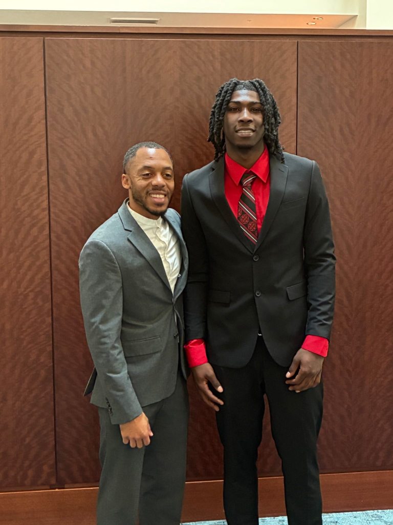 Corien Coleman stands in a suit next to his coach
