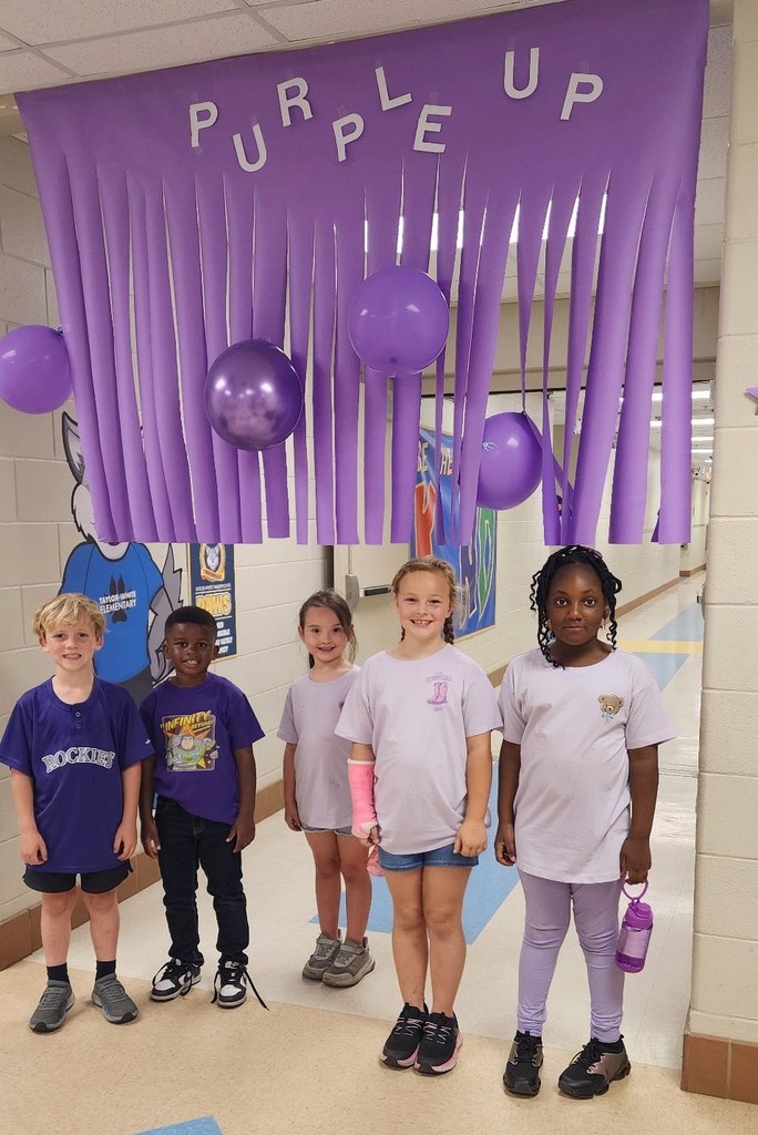 Five students wearing purple shirts, standing under a banner that reads "Purple Up"