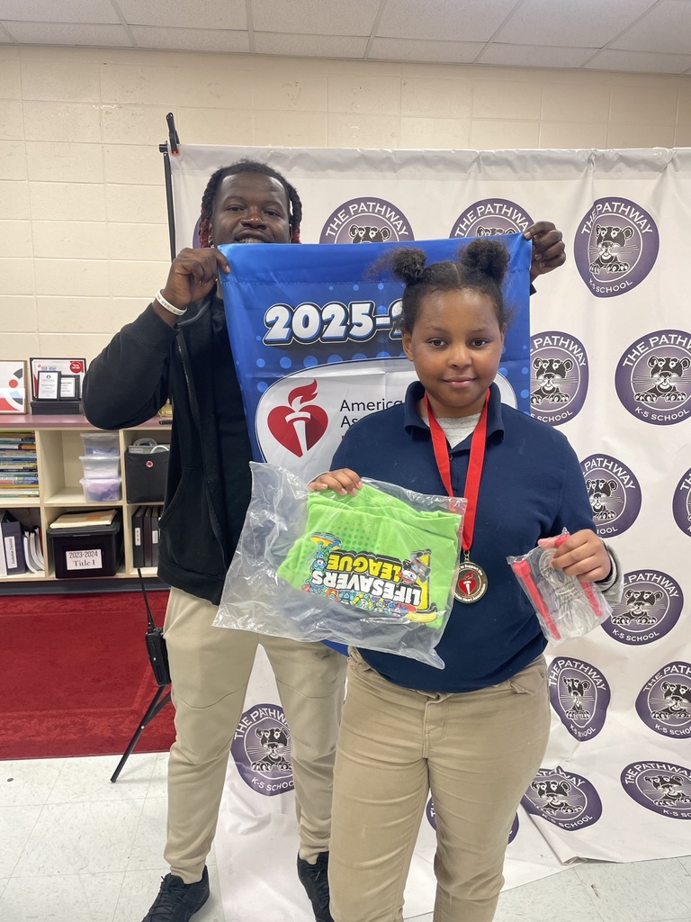 Students standing with the PE coach. The coach is holding a banner that read "American heart Association Kids Heart Challenge". The  students are holding up rewards they've earned for completing the challenge 