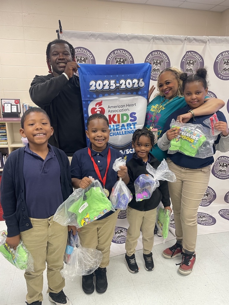 Students standing with the PE coach. The coach is holding a banner that read "American heart Association Kids Heart Challenge". The  students are holding up rewards they've earned for completing the challenge 