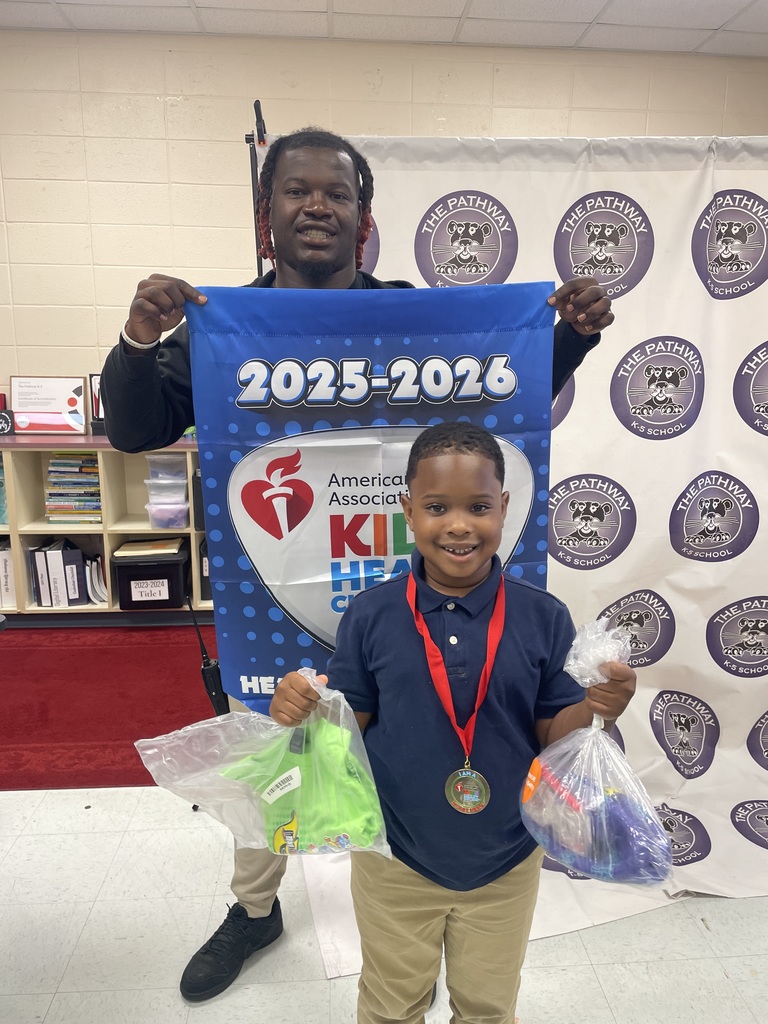 Students standing with the PE coach. The coach is holding a banner that read "American heart Association Kids Heart Challenge". The  students are holding up rewards they've earned for completing the challenge 