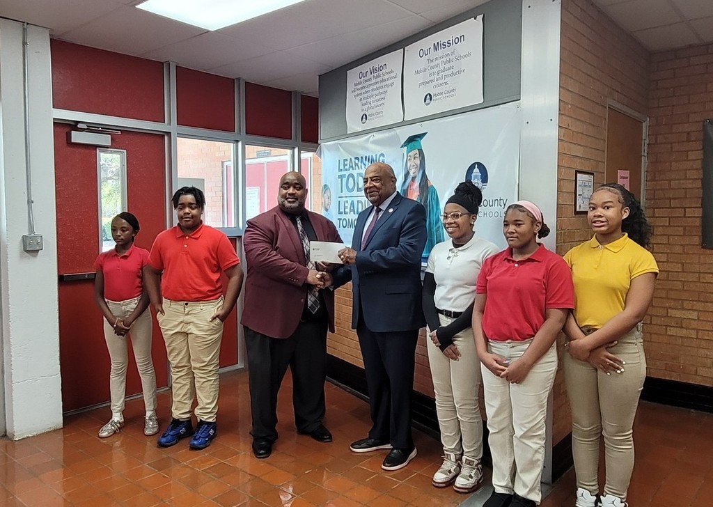 Sam Jones gives a check to Booker T. Washington Middle School's principal, Mr. Williams. Five students are standing beside them.