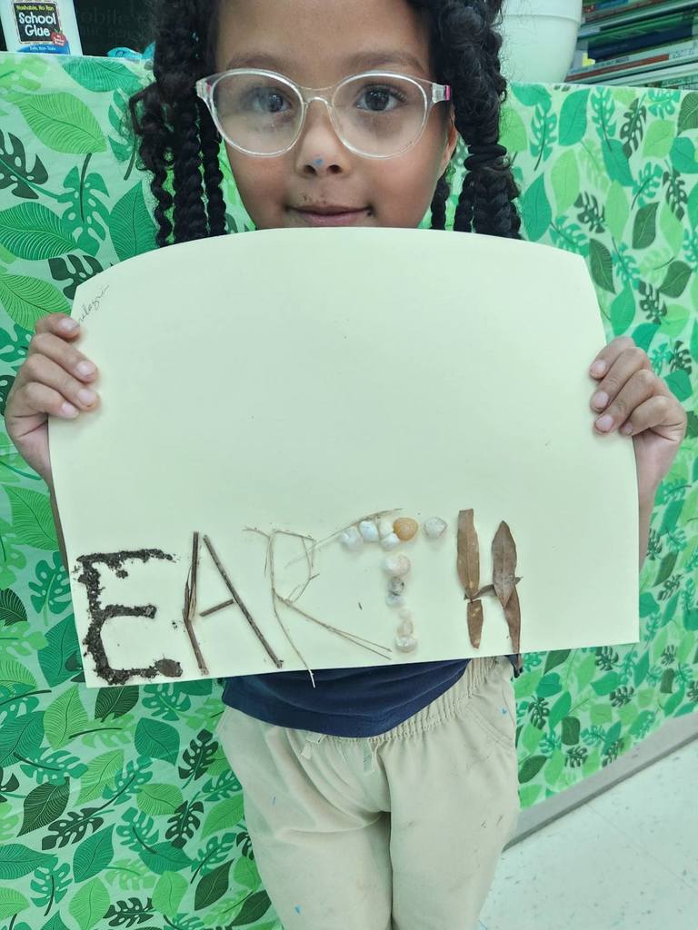 A girl holding a piece of paper with the word "Earth" made with sticks and stones