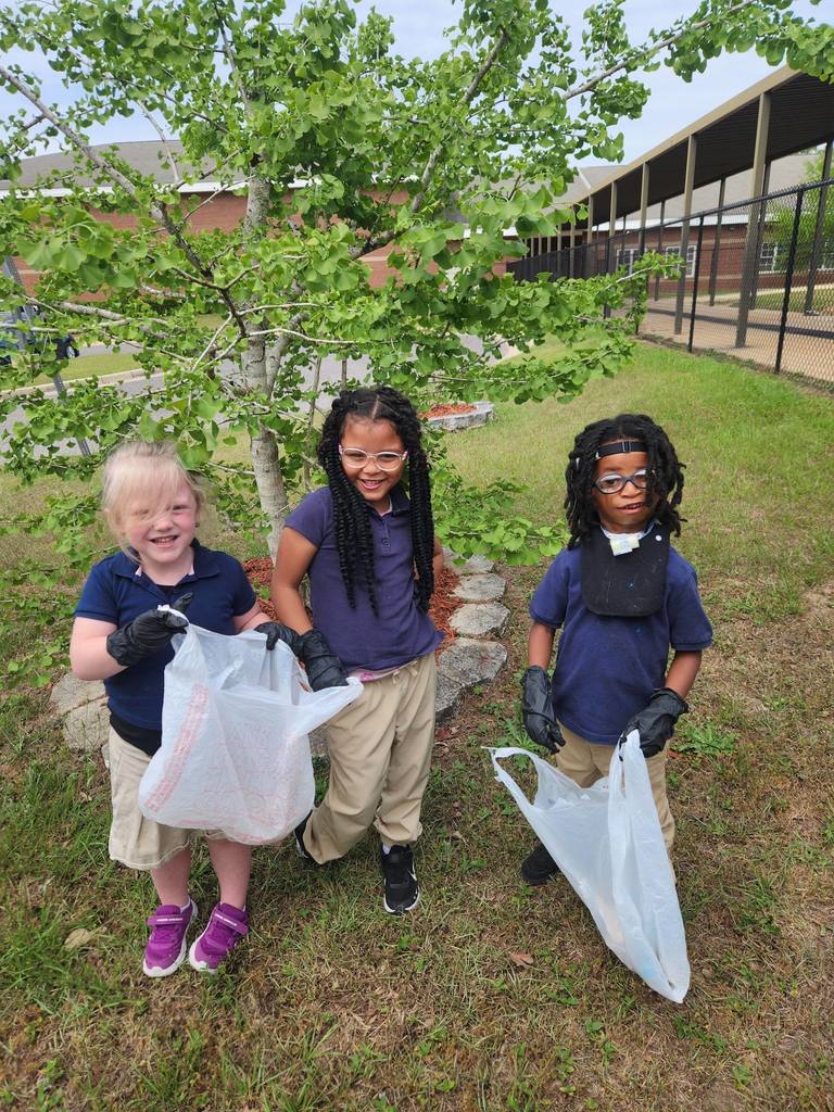 Three Callahan students standing outside, holding trash bags