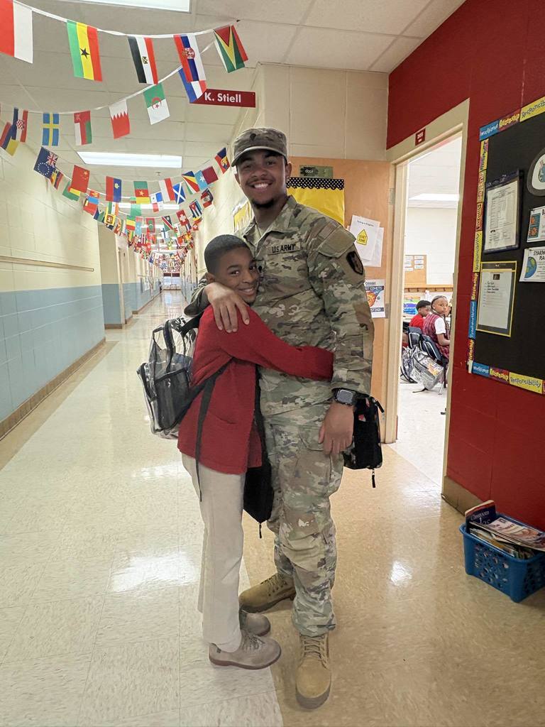 A boy in a red sweater hugging a man in U.S. Army fatigues