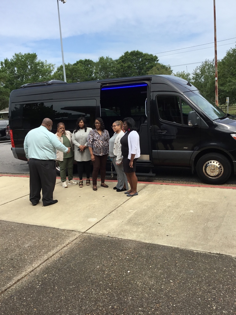 Booker T. Washington Middle School's principal and office staff are standing in front of the limousine . Mr. Williams, principal, reads the lunch plans to the office staff.