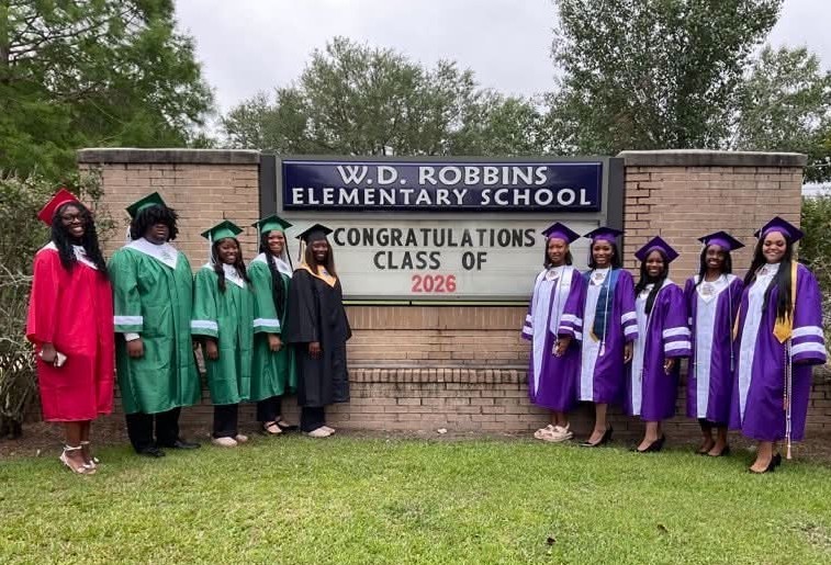A group of seniors in caps and gowns standing in front of the Robbins Elementary sign