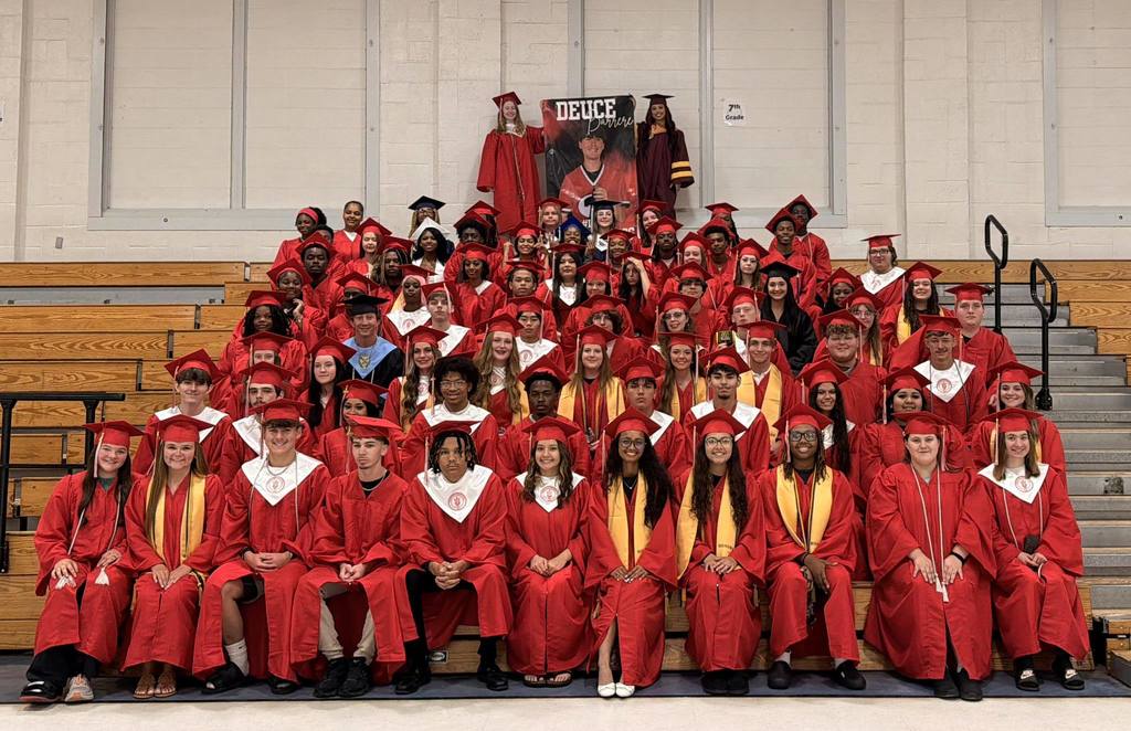 A large group of seniors, most in red caps and gowns, in a group photo in a gymnasium