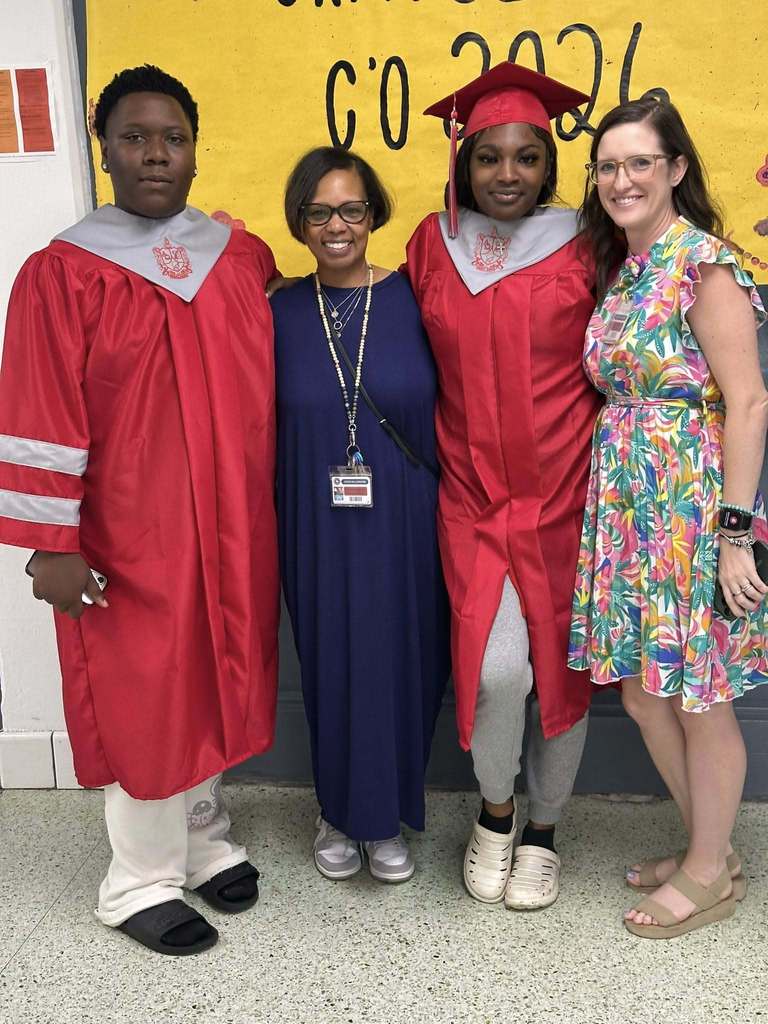 Two seniors in red caps and gowns stand with two teachers