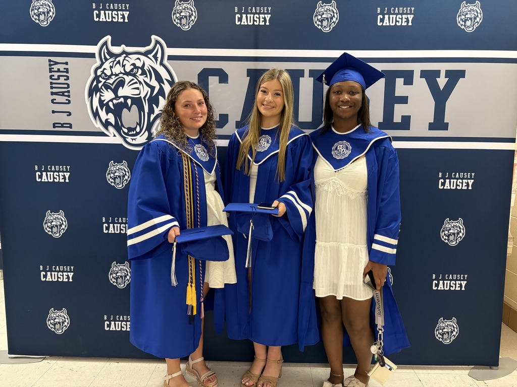 Three seniors in blue caps and gowns stand in front of a Causey Middle School backdrop