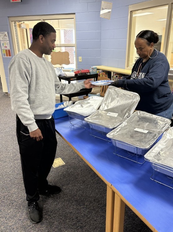 Mrs. Ray scooping food onto a plate for one of our PE coaches 