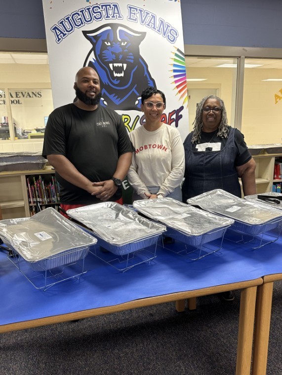 Mrs. Kidd with the caterer and speech therapist in a group photo in front of the food before serving to the staff 
