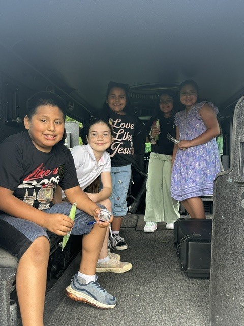 A group of children sit in the back of a vehicle. Three are in the front row, two are in the back.