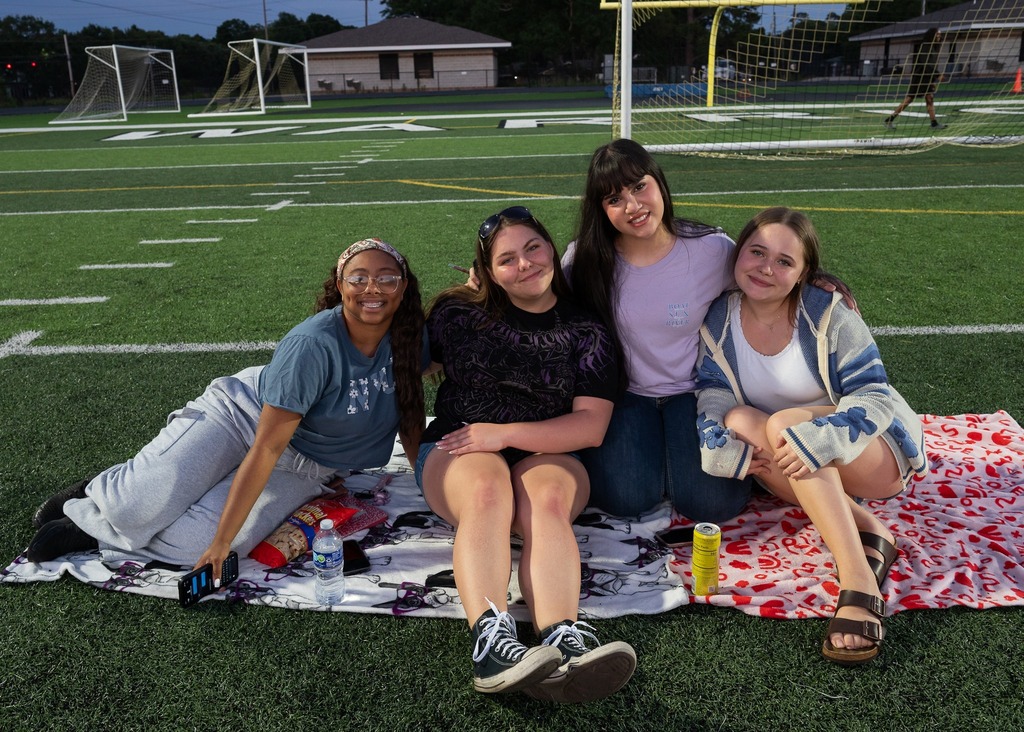 Four Davidson students sitting on a blanket on the football field