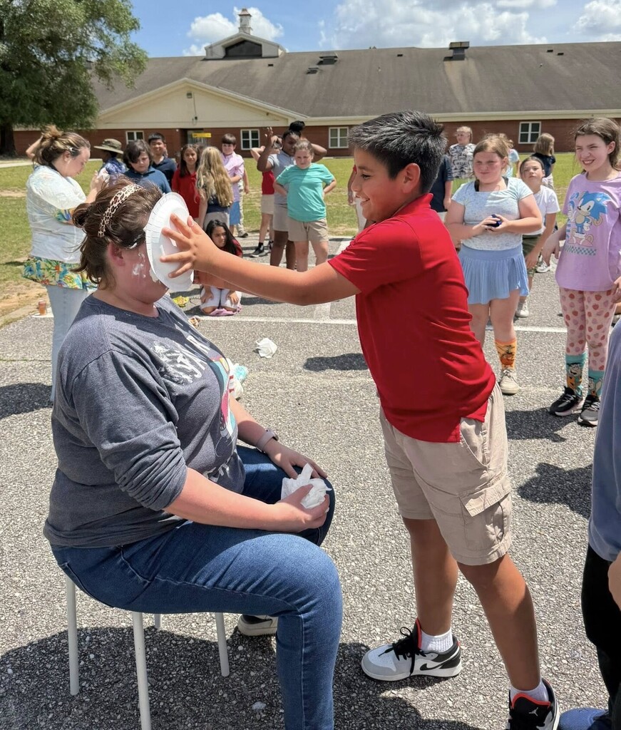 A student puts a pie into the face of a teacher
