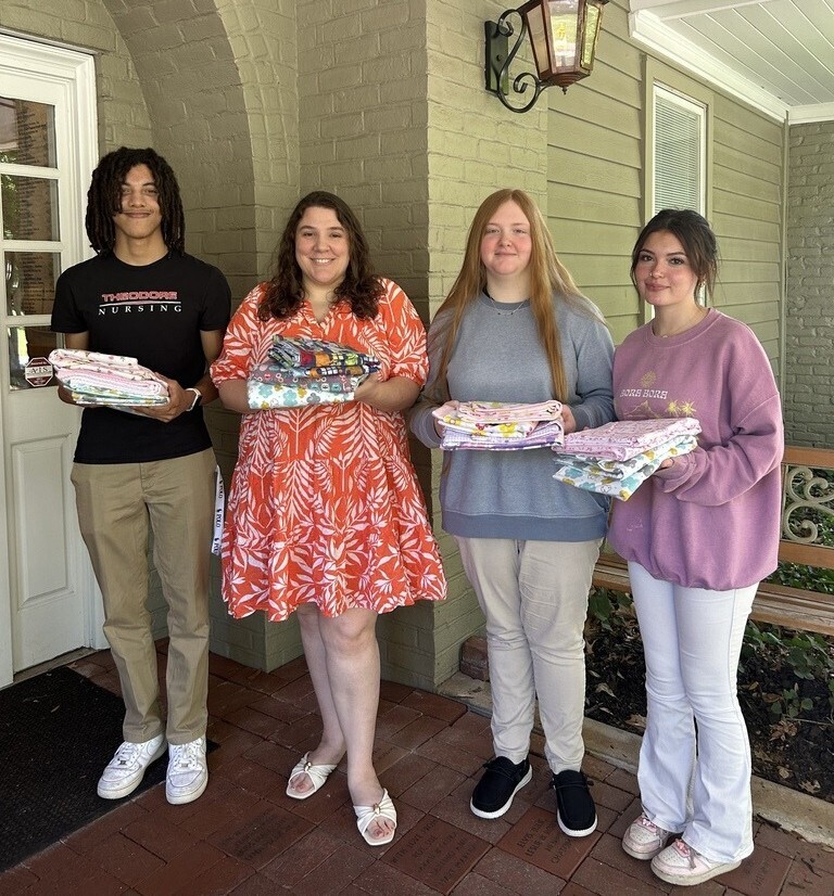 Three Theodore High students and a Ronald McDonald House employee, holding blankets