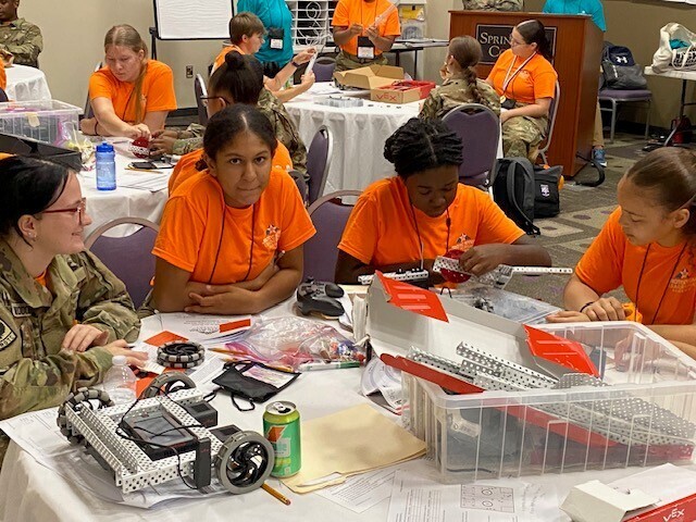 Four cadets in orange shirts working on a robot at a table